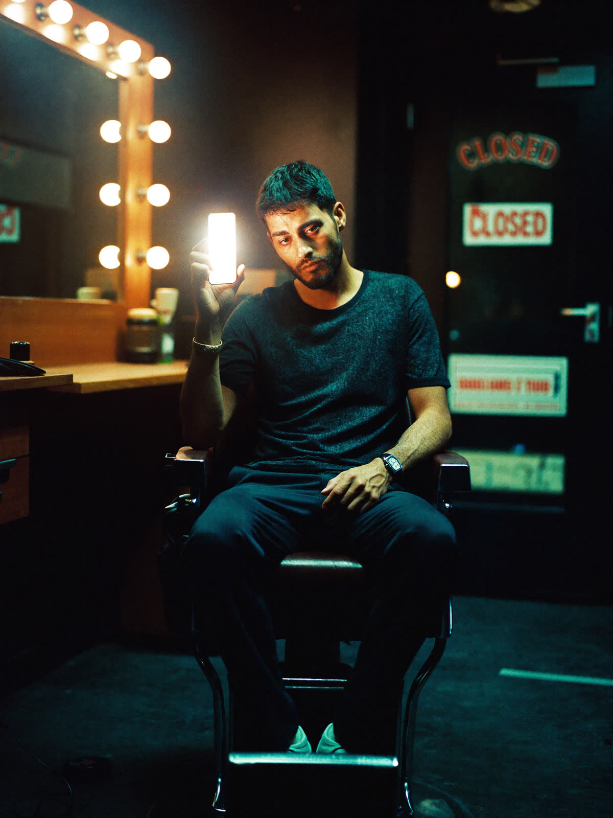 A barber alone in his closed shop at night, looking at a blank phone screen
